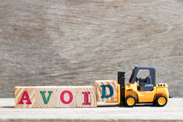 Toy forklift hold letter block d to complete word avoid on wood background