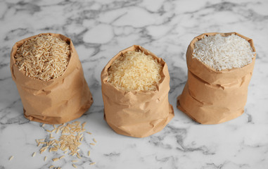 Paper bags with different types of rice on marble background