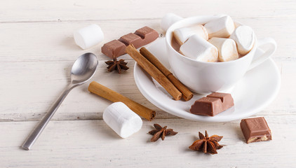 a cup of hot chocolate with marshmallow and spices on white wooden background. close up.