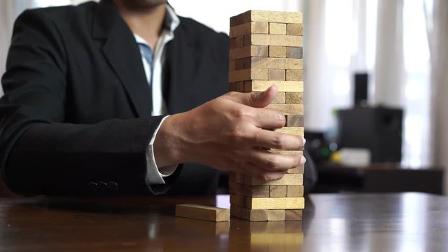 Hand of businessman pulling wood block fail on building tower at home