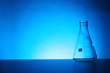 Empty conical flask on table against color background. Chemistry laboratory glassware