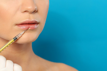 Young woman getting lips injection on color background, space for text. Cosmetic surgery
