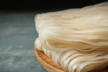 Plate with raw rice noodles on wooden table, closeup. Space for text