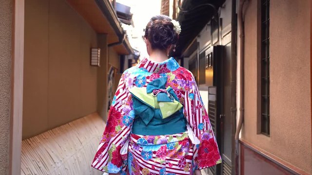 fast forward of young japanese girl in kimono dressing walking in the path to festival. back view lady in colorful beautiful traditional costume going pass by the house wooden door in hanamikoji dori