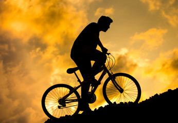 Naklejka premium Silhouette of a boy riding a mountain bike at sunset