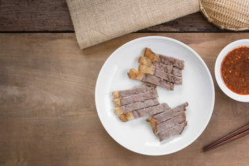 top view of sliced grilled beef in a ceramic dish served with spicy sauce on wooden table. asian homemade style food concept.