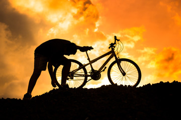 Silhouette of a boy fixing a mountain bike at sunset