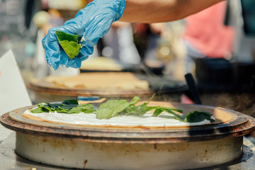 Fototapeta na wymiar Cook's hand putting arugula on a crepe while cooking next to others