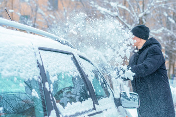 adult male removing snow from car roof with brush in winter season