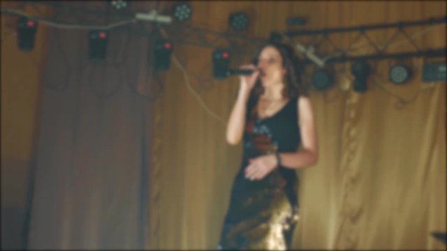 singer girl brunette sings blurred background night beautiful light with microphone. slow motion video. Singer in silhouette. Frontman woman silhouette singing to the microphone to the crowd on a
