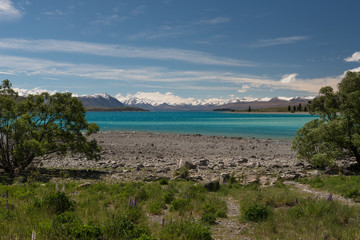 The view across a low Lake Tekapo with a stoney beach in the foreground and the snow capped Southern Alps in the background. In the Mackenzie Basin, New Zealand.