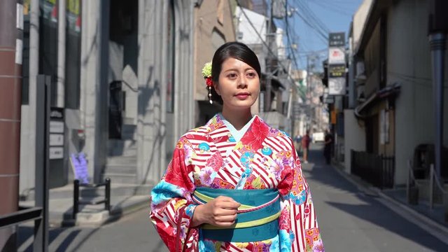local japanese lady with flower accessories on head wearing kimono costume walking on the city urban street. beautiful woman in colorful traditional dress going to join summer festival alone.