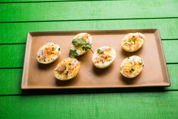 Fried hot boiled egg masala is a popular healthy breakfast or starter menu from India. With onion, coriander, black pepper, tomato and salt sprinkled over half of eggs