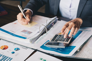 Business woman using calculator and laptop for do math finance on wooden desk in office and...