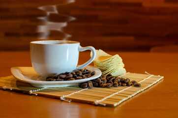 A cup of hot coffee in white cup with steaming and coffee bean and potato chips