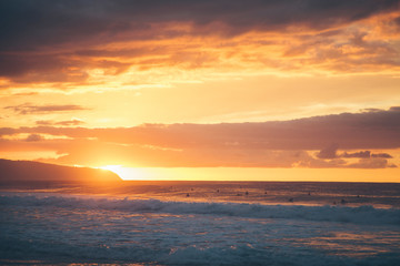 The sunsets over the North Shore of Oahu Hawaii while surfers ride waves