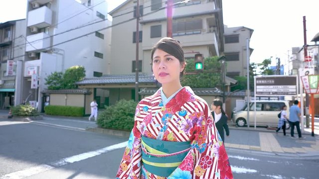 cute girl student waving hands goodbye in background. young elegant japanese local woman walking on zebra crossing wearing flower pattern kimono in city kyoto japan in summer. asia travel culture.