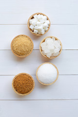 Various types of sugar on white wooden background.