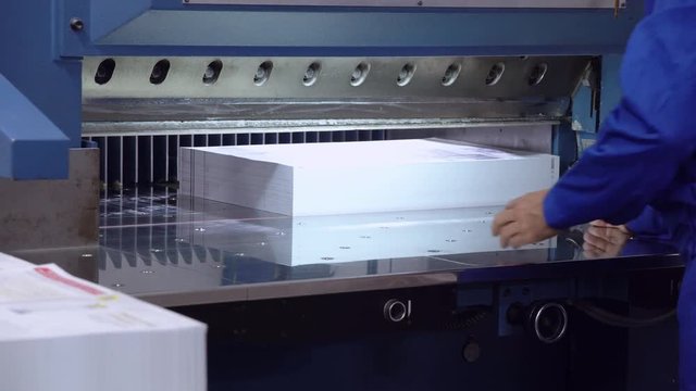 employee working typography unrecognizable male wearing blue uniform works with print equipment stack of paper on the conveyor