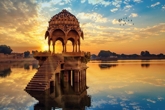 Ancient architecture ruins at Gadi Sagar (Gadisar) lake Jaipur Rajasthan at sunrise with vibrant moody sky. 