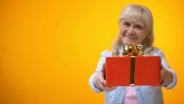 Optimistic senior lady showing present to camera, preparation for holidays