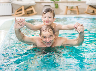 Happy grandfather having fun with his grandson in the pool