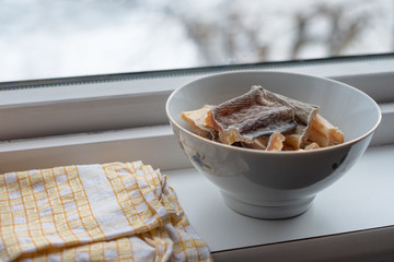 Skin cod fish drying fresh in ceramic bowl with table wipes on window sill in winter