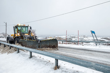 Yellow snowplough plowing on snowy road