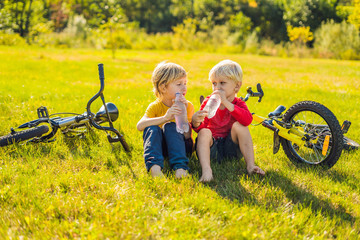 Two little boys drink water in the park after riding a bike