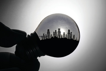 An incandescent light bulb with view of mining oil rigs of a sandy coast for the concept of energy...