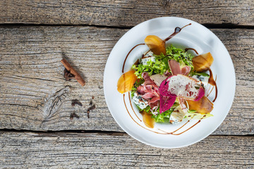 Salad with slices of bacon, persimmon and pieces of gorgonzola is beautifully presented on a white plate