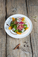 Salad with slices of bacon, persimmon and pieces of gorgonzola is beautifully presented on a white plate