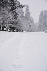 Snowy winter road with tire traces on the snow and cleaned walkway on the side