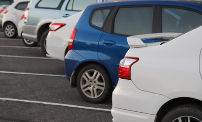 Closeup of rear or back side of white car with other cars parking in parking area in twilight evening. 