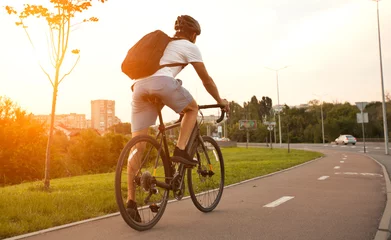Foto auf Acrylglas Fahrräder Der junge Mann in Freizeitkleidung ist in der Abendstadt mit dem Fahrrad unterwegs