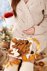 pregnant woman sitting near the window and drinking tea, beautiful winter landscape with snowy forest is outside the window, christmas decoration