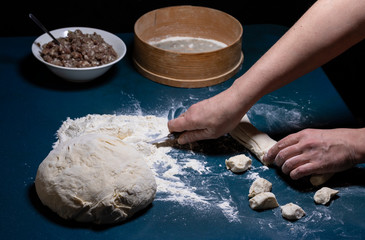 Women's hands cut the dough into pieces on the table.