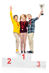 happy kids with medals and trophy cup standing on winner pedestal, shouting and looking at camera...