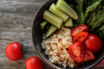 Bowl with porridge and fresh vegetables on wooden table. Diet food