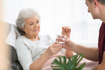 Obraz na płótnie Canvas Man giving pill to elderly woman, indoors