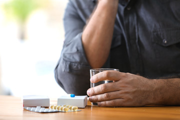 Mature man with different pills and glass of water at table