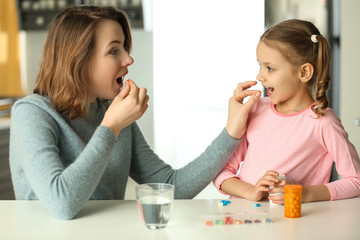 Young woman and daughter taking pills at table