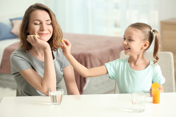 Little daughter giving pill to her mother at home