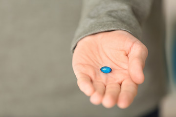 Young man holding blue pill, closeup