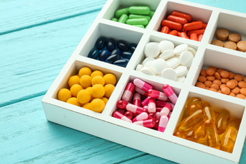 Divided box with different pills on wooden background