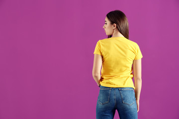 Young woman in stylish t-shirt on color background, back view