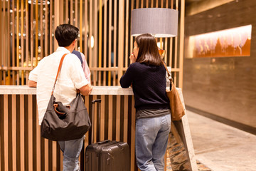 Asian couple with suitcase checking in at hotel reception.