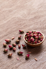 Pink red dried rose buds in wooden bowl with petals on old wooden background.
