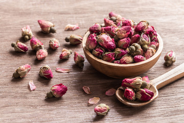 Pink red dried rose buds in wooden bowl with petals on old wooden background.