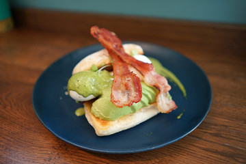 Fresh baked bread with fresh avocado and avocado sauce serving with sliced fried bacon on top